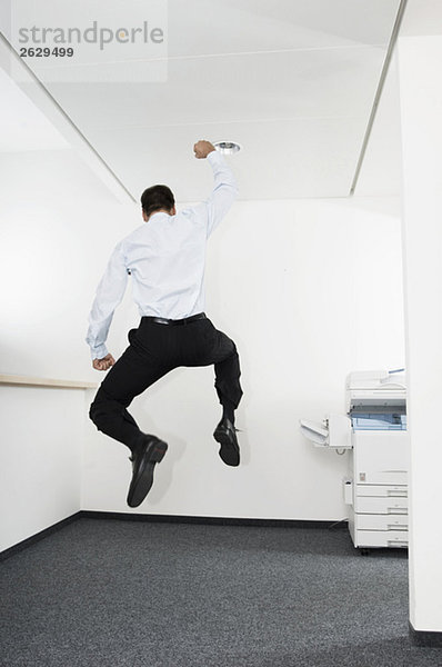 Geschäftsmann beim Luftspringen im Büro  Rückansicht