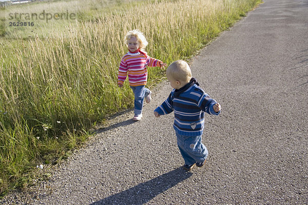 Kleines Mädchen (2-3) und Junge (1-2) laufen über den Weg