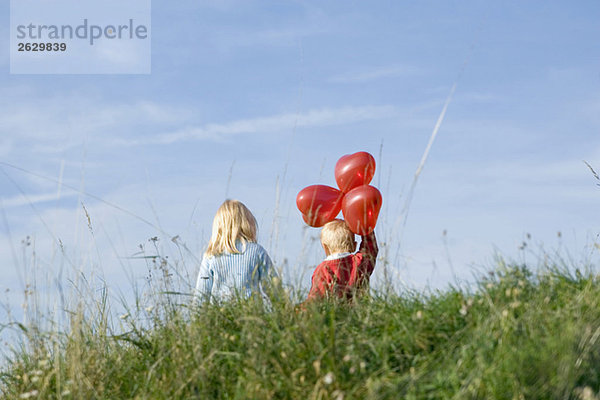 Kleines Mädchen und Junge (3-4) mit Ballons  die Hand in Hand gehen  Rückansicht