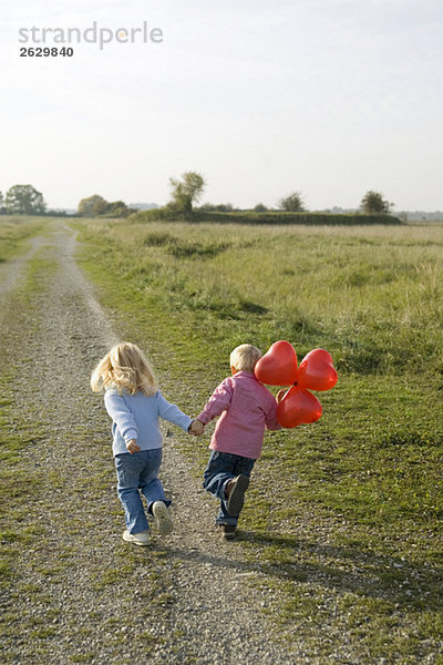Kleiner Junge und Mädchen (3-4) mit über den Feldweg laufenden Ballons  Rückansicht