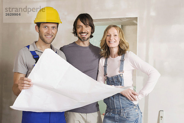 Junges Paar und Bauarbeiter mit Bauplan  lächelnd  Portrait