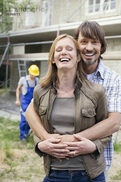 Young couple at site embracing  construction worker in background