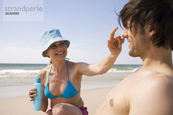 Deutschland  Ostsee  Junges Paar am Strand  Frau trägt Sonnencreme auf die Nase des Mannes auf