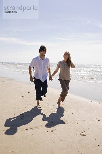 Deutschland  Ostsee  Junges Paar am Strand entlang  Händchen haltend
