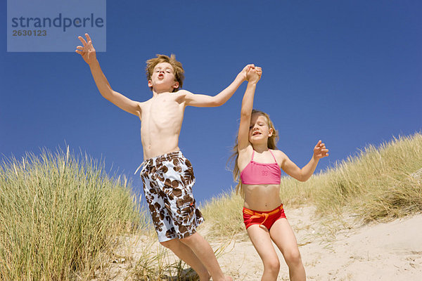 Deutschland  Ostsee  Junge (8-9) und Mädchen (6-7) springen die Stranddüne hinunter.