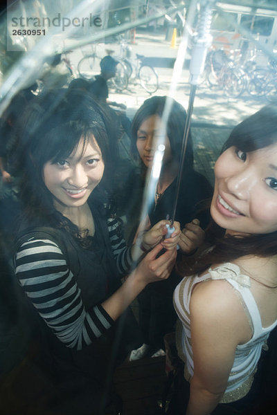 Junge erwachsene Freunde stehen zusammen unter einem Regenschirm und lächeln in die Kamera.
