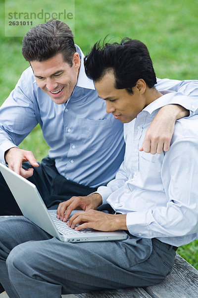 Geschäftspartner  die den Laptop gemeinsam im Freien benutzen  der eine Arm um die Schulter des anderen.