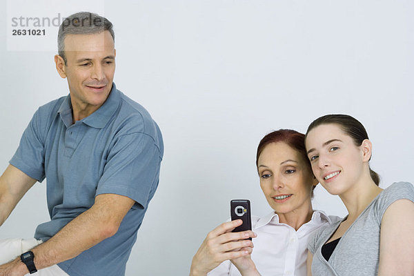 Familie sitzt zusammen  Eltern schauen aufs Handy  Tochter lächelt in die Kamera