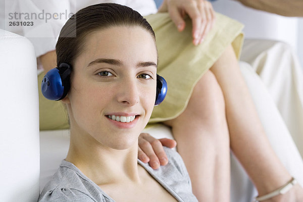 Teenagermädchen hört Kopfhörer  lächelt in die Kamera  Frauenhand auf der Schulter