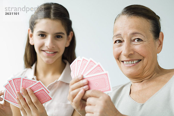 Großmutter und Enkelin spielen Karten und lächeln in die Kamera.