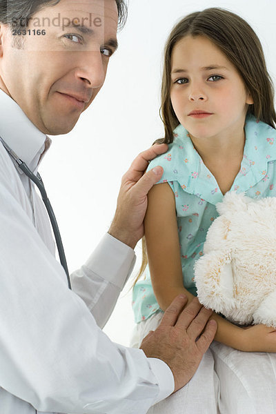 Kinderarzt tröstendes kleines Mädchen  lächelnd über die Schulter vor der Kamera