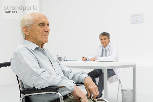 Senior-Patient im Rollstuhl  Arzt am Schreibtisch im Hintergrund