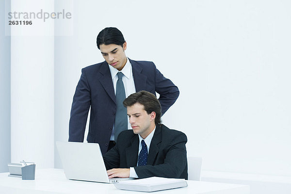 Geschäftsmann mit Laptop am Schreibtisch  Kollege wacht über seine Schulter