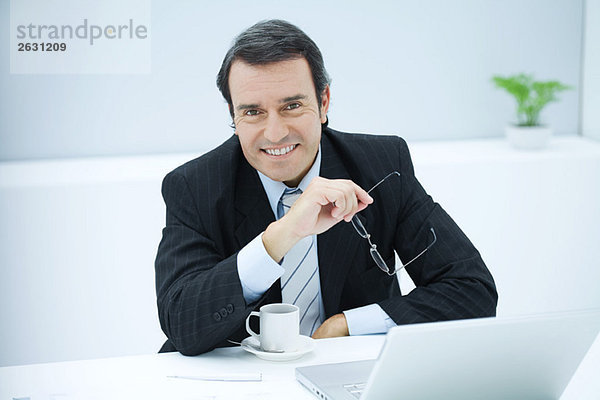 Geschäftsmann am Schreibtisch sitzend mit Kaffeetasse  lächelnd vor der Kamera