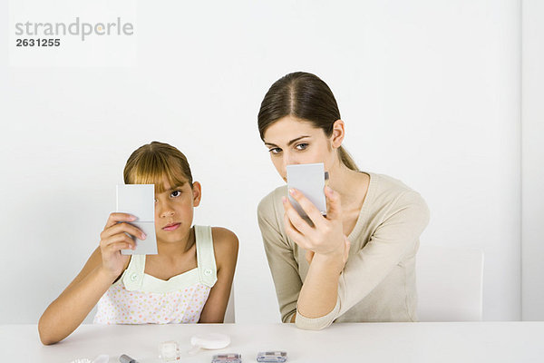 Mädchen und junge Frau sitzen Seite an Seite  schauen in Handspiegel  Kosmetik im Vordergrund