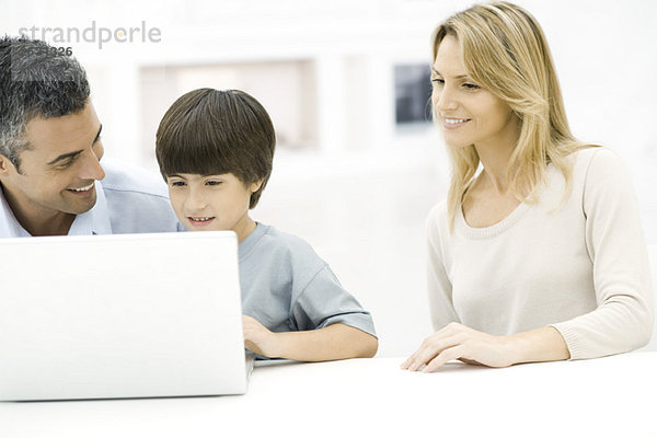 Vater und Sohn benutzen gemeinsam einen Laptop  Mutter schaut zu.