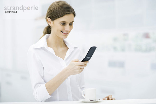 Frau steht am Küchentisch  schaut auf das Handy  lächelt