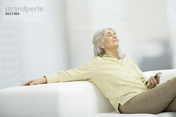 Seniorenfrau beim Musikhören  auf der Couch sitzend mit geschlossenen Augen