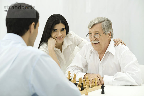 Menschen spielen Schach  Frau sitzt mit der Hand auf der Schulter des älteren Mannes.