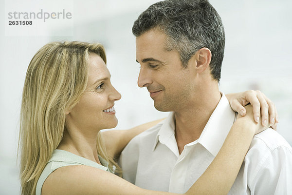 Ein Paar lächelt sich an  eine Frau wickelt die Arme um den Mann.