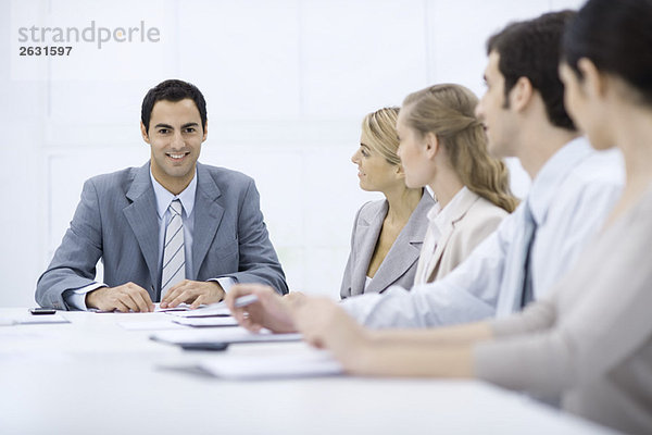 Geschäftsmann sitzend mit Kollegen am Konferenztisch  lächelnd vor der Kamera