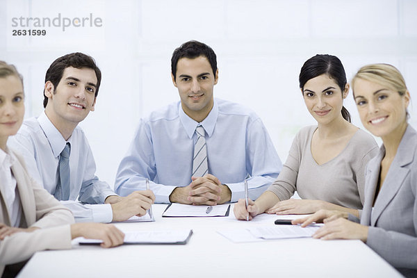 Geschäftsmann sitzend mit Kollegen am Konferenztisch  lächelnd vor der Kamera