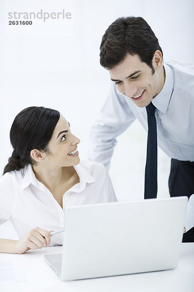 Professionelle Frau sitzend mit Laptop  männlicher Kollege schaut ihr über die Schulter  beide lächelnd
