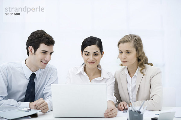 Drei Profis  die gemeinsam auf den Laptop schauen  lächelnd