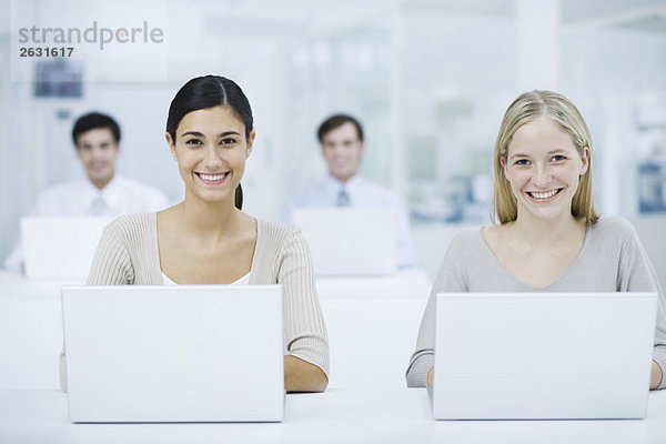 Professionelle Frauen  die Laptops benutzen  lächeln in die Kamera  Kollegen im Hintergrund