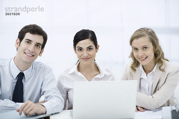 Team von Profis sitzt mit Laptop-Computer  lächelnd vor der Kamera