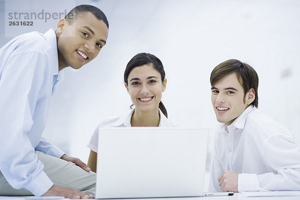Junge Profis versammelten sich um Laptop-Computer  lächelnd vor der Kamera