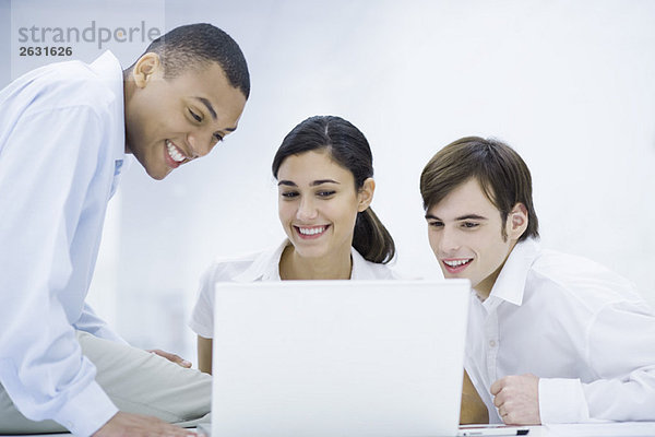 Junge Profis  die gemeinsam auf den Laptop schauen  lächelnd