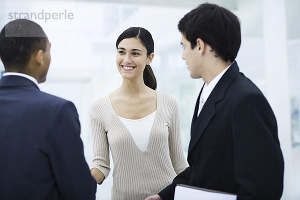 Professionelle Frau steht mit zwei Geschäftsleuten  schüttelt einem Mann die Hand  lächelt