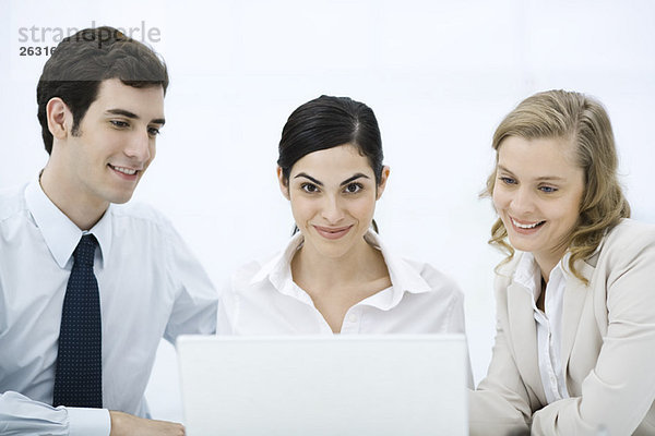 Drei Profis versammelten sich um Laptop-Computer  Frau in der Mitte lächelnd in der Kamera