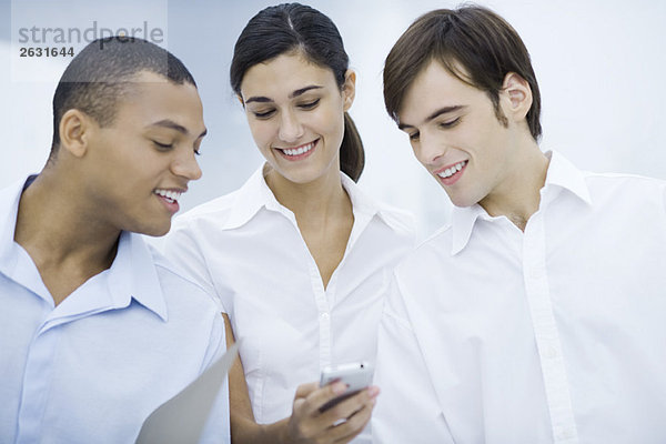 Drei junge Profis  die gemeinsam das Handy anschauen  lächelnd
