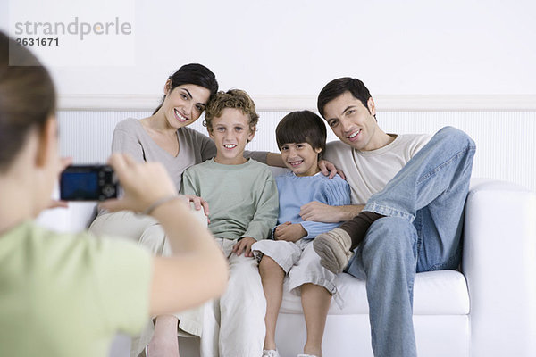Junges Mädchen fotografiert ihre Eltern und Brüder  die zusammen auf dem Sofa sitzen