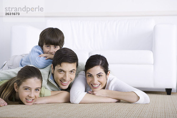 Familie liegt zusammen auf dem Boden  Sohn liegt auf dem Rücken seines Vaters  alle lächelnd vor der Kamera.