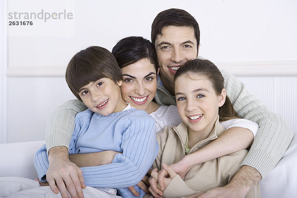 Vater umarmt seine Frau und zwei Kinder  alle lächelnd vor der Kamera.