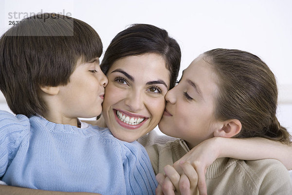 Mutter wird von Tochter und Sohn auf jede Wange geküsst  lächelnd.