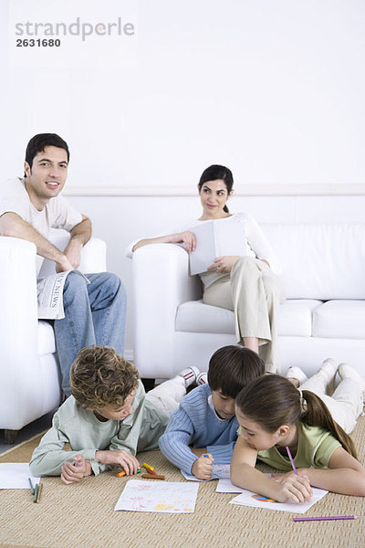 Familie entspannt sich gemeinsam im Wohnzimmer  Kinder malen auf dem Boden  Vater lächelt in die Kamera