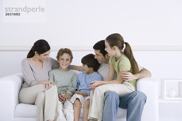 Familie mit drei Kindern  die zusammen auf dem Sofa sitzen  ein Junge lächelt vor der Kamera.