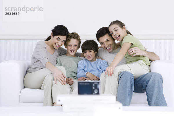 Familie sitzt zusammen auf Sofa  posiert für Digitalkamera im Vordergrund