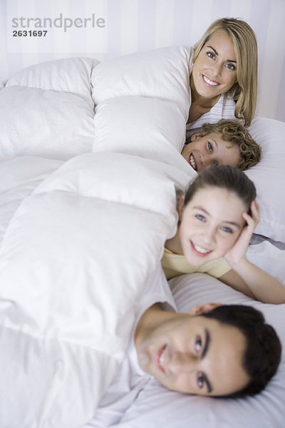 Familie zusammen im Bett liegend  lächelnd vor der Kamera