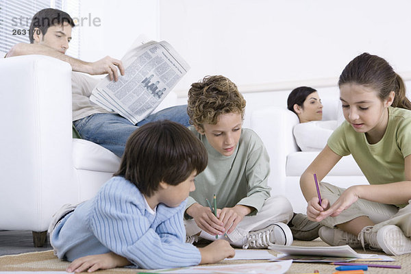Drei Kinder sitzen auf dem Boden  malen  Eltern lesen im Hintergrund