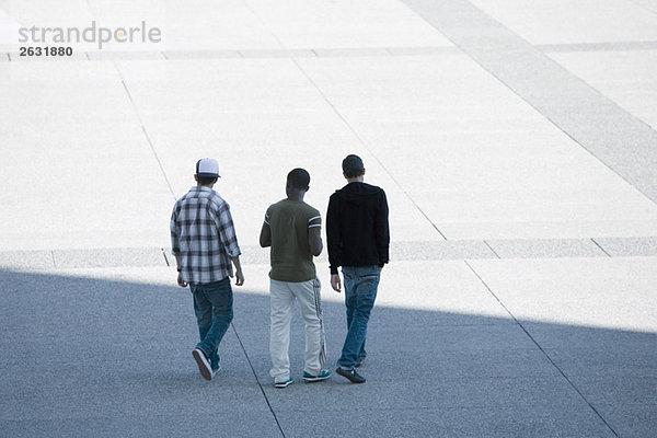 Drei junge Männer gehen zusammen über den öffentlichen Platz.