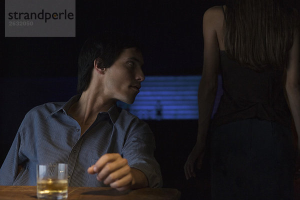 Glas Whiskey auf dem Tisch  Mann sitzt und schaut weg  Rückansicht der Frau im Dunkeln stehend