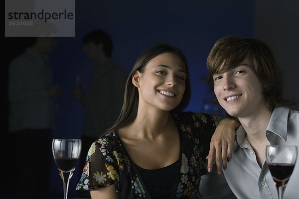 Paar lächelt in die Kamera  Weingläser im Vordergrund  Portrait