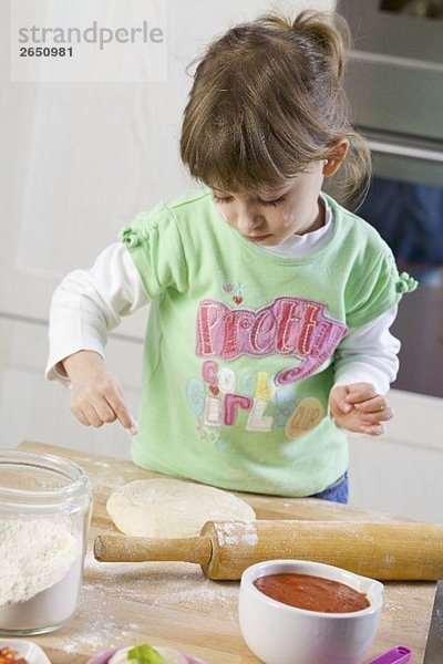 Kleines Mädchen bestäubt Pizzateig mit Mehl