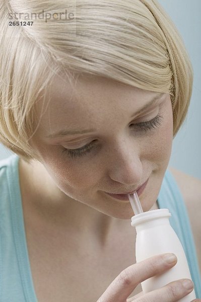 Junge  blonde Frau trinkt mit Strohhalm aus Plastikflasche