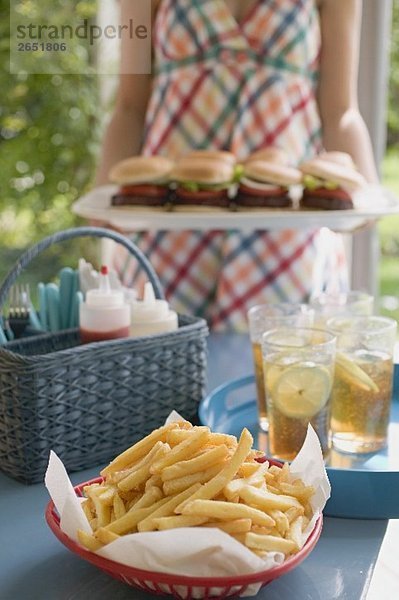 Pommes frites und Eistee auf Tisch  Frau serviert Hamburger